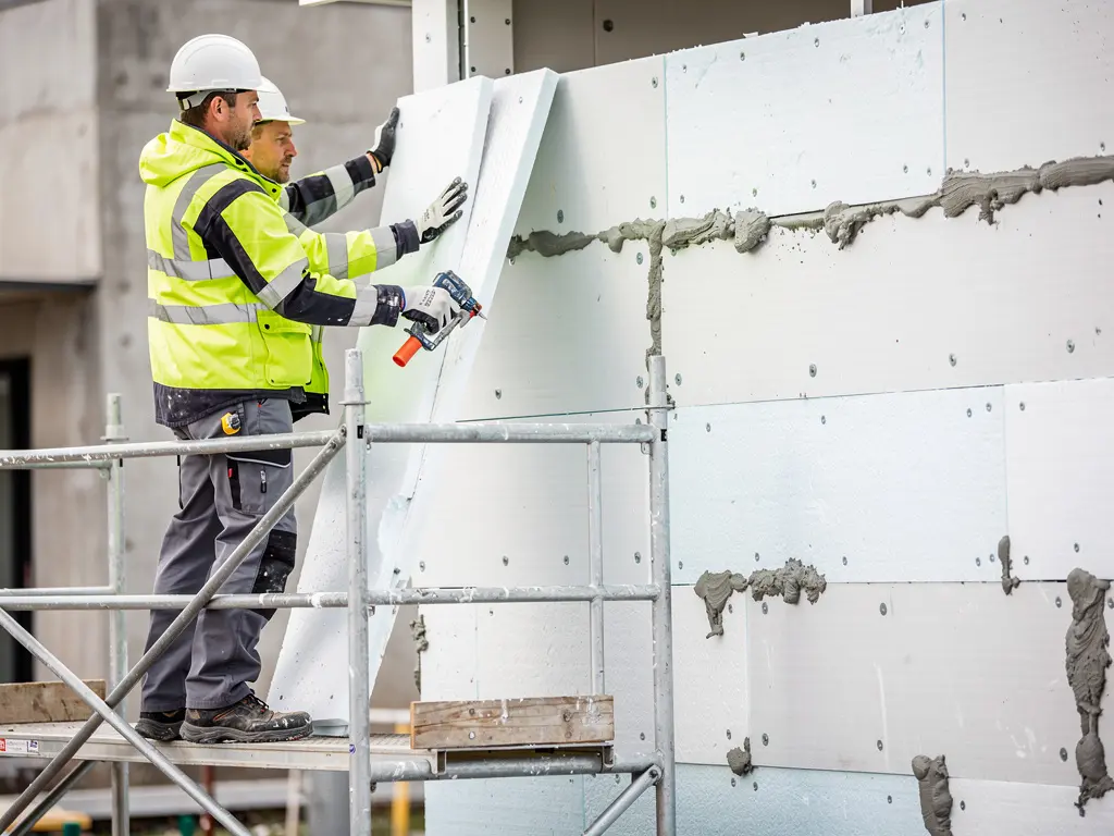 Pose de panneaux isolants rigides sur un mur depuis l'échafaudage de chantier